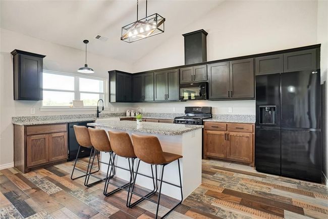 Kitchen with pendant lighting, black appliances, wood-type flooring, a kitchen island, and high vaulted ceiling | Image 12