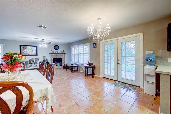 Dining room featuring french doors, a brick fireplace, a chandelier, a ceiling fan, and light tile patterned flooring | Image 9