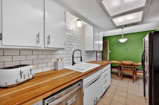 Kitchen with butcher block countertops, freestanding refrigerator, stainless steel dishwasher, decorative backsplash, and a textured ceiling | Image 10