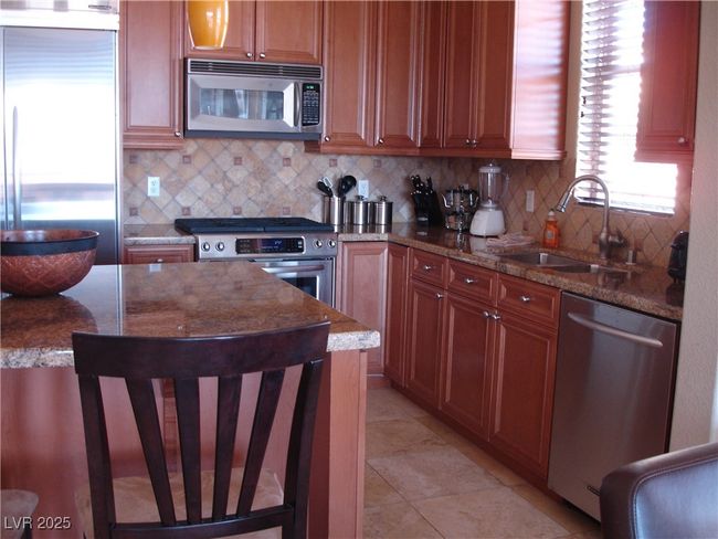 Kitchen with stainless steel appliances, a sink, backsplash, and stone countertops | Image 9
