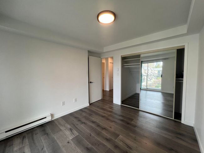 Unfurnished bedroom with a baseboard radiator, dark wood-style floors, and a closet | Image 24