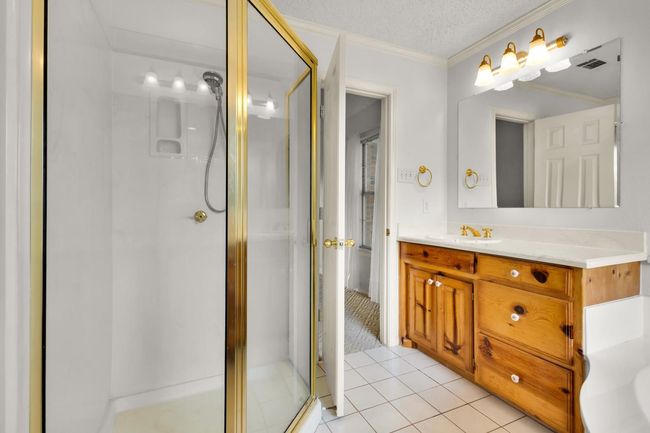 Bathroom featuring a shower stall, vanity, tile patterned floors, ornamental molding, and a textured ceiling | Image 17