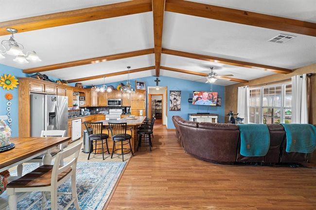 Living room with ceiling fan with notable chandelier, vaulted ceiling with beams, light wood finished floors, and visible vents | Image 19
