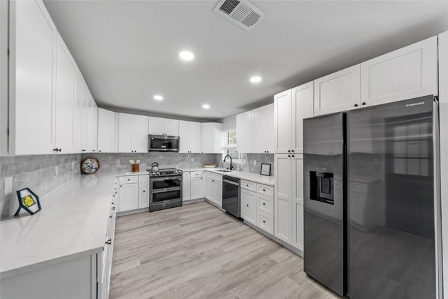Kitchen featuring stainless steel appliances, light wood finished floors, recessed lighting, tasteful backsplash, and white cabinetry | Image 7
