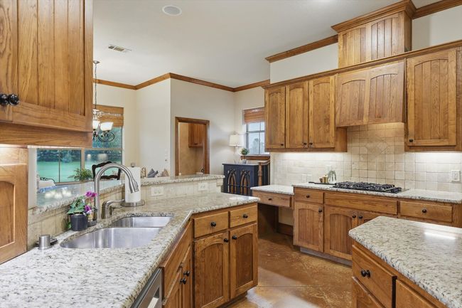 Kitchen featuring tasteful backsplash, crown molding, light stone countertops, and brown cabinetry | Image 15