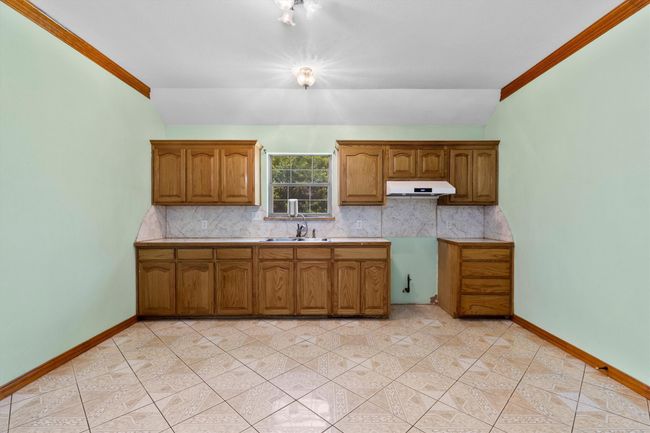 Kitchen with under cabinet range hood, a sink, backsplash, brown cabinets, and crown molding | Image 23