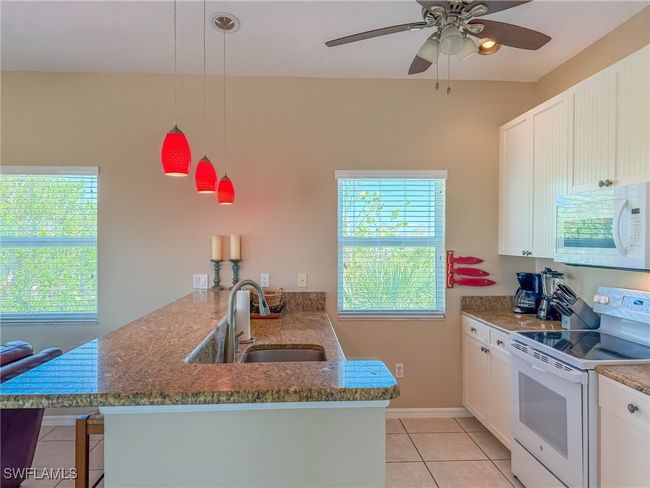Kitchen with light tile patterned floors, white cabinetry, a sink, white appliances, and a peninsula | Image 13