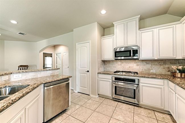 Kitchen with stainless steel appliances, decorative backsplash, arched walkways, light stone counters, and recessed lighting | Image 23