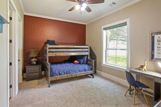 This Secondary Bedroom comes equipped with crown molding, plush carpeting, an accent wall, large walk-in closet, and ensuite bathroom. The cased window overlooks the Front Yard and is shaded by the majestic oak tree. | Image 35