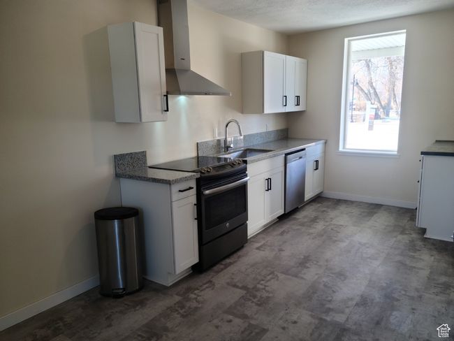 Kitchen featuring wall chimney range hood, electric range, stainless steel dishwasher, a sink, and white cabinets | Image 6