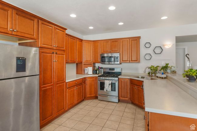 Kitchen featuring a sink, light tile patterned floors, brown cabinetry, light countertops, and appliances with stainless steel finishes | Image 17