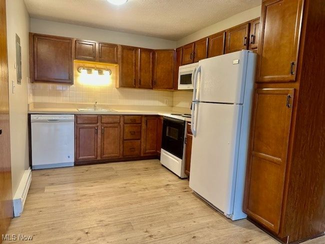 Kitchen featuring light wood finished floors, a sink, white appliances, light countertops, and decorative backsplash | Image 9