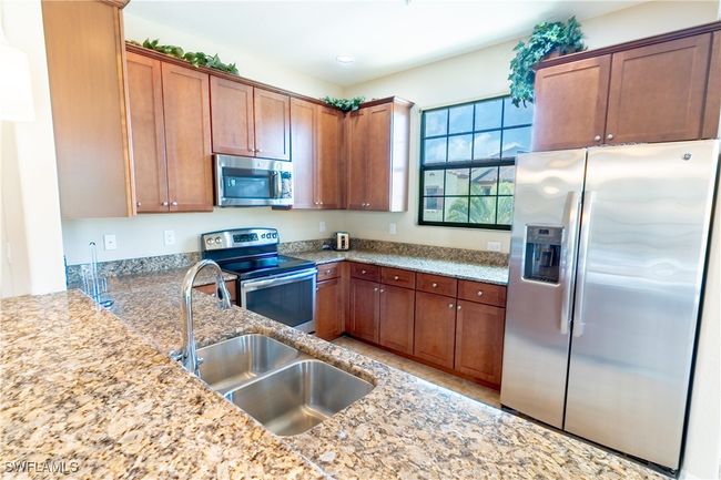 Kitchen featuring light stone countertops, recessed lighting, appliances with stainless steel finishes, a sink, and brown cabinets | Image 10