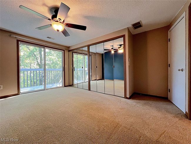 Master bedroom with light carpet, a textured ceiling, access to outside, multiple closets, and a ceiling fan | Image 10