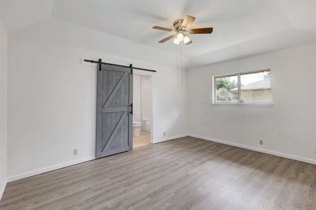 Empty room featuring a ceiling fan, a barn door, wood finished floors, and baseboards | Image 11