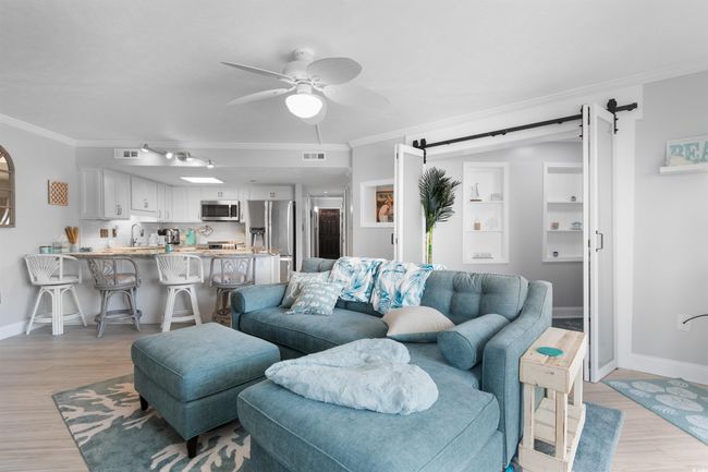 Living area with a barn door, crown molding, baseboards, ceiling fan, and light wood finished floors | Image 11