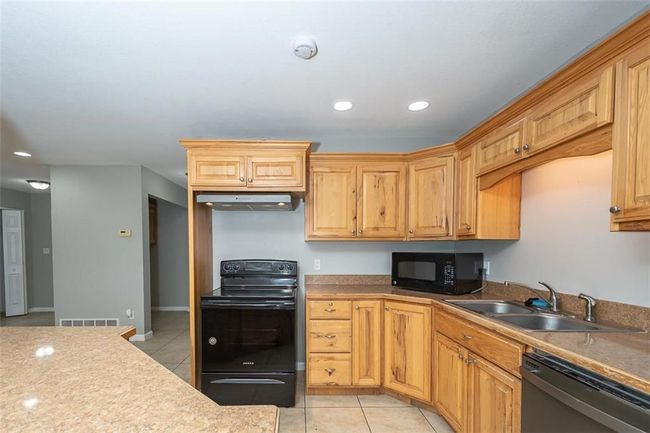 Kitchen featuring visible vents, under cabinet range hood, light tile patterned floors, black appliances, and a sink | Image 16