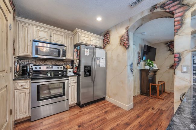 Kitchen featuring cream cabinetry, light wood-type flooring, visible vents, dark countertops, and appliances with stainless steel finishes | Image 11