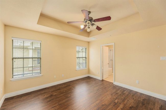 Empty room featuring a tray ceiling, dark wood-style flooring, and a ceiling fan | Image 14