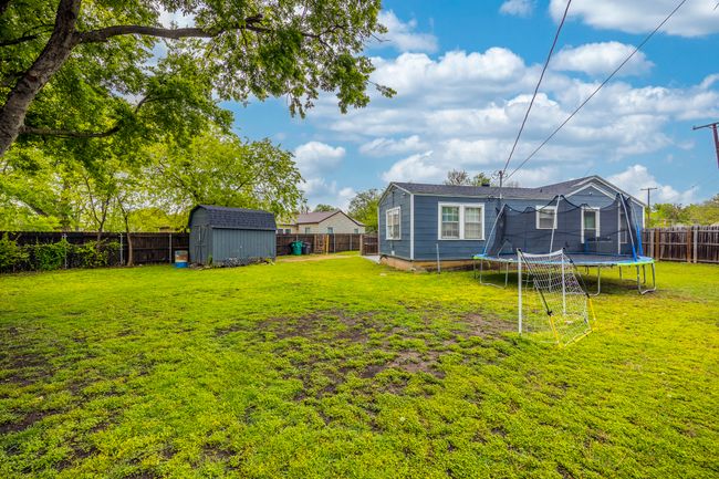 View of yard featuring a trampoline, a storage unit, a fenced backyard, and an outbuilding | Image 25