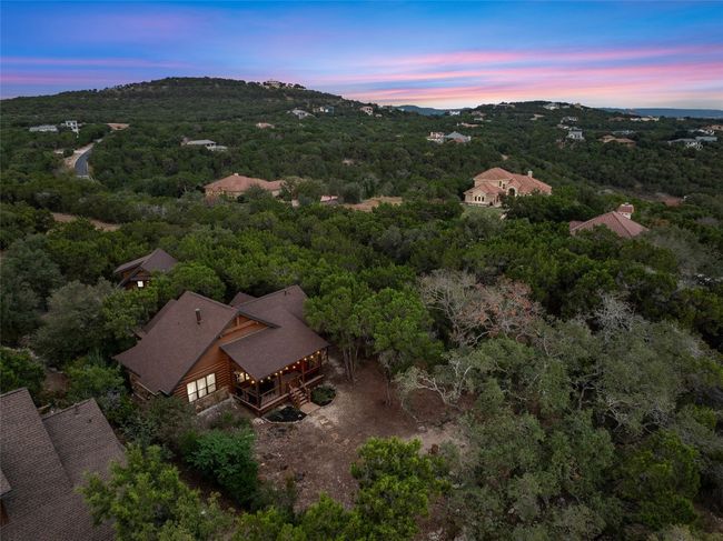 Aerial view at dusk showcasing the cozy home nestled among dense greenery. The back deck and surrounding foliage highlight the secluded charm of the property in its tranquil setting | Image 37