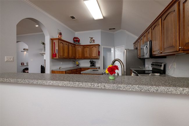 Kitchen with brown cabinets, a peninsula, stainless steel appliances, and visible vents | Image 15