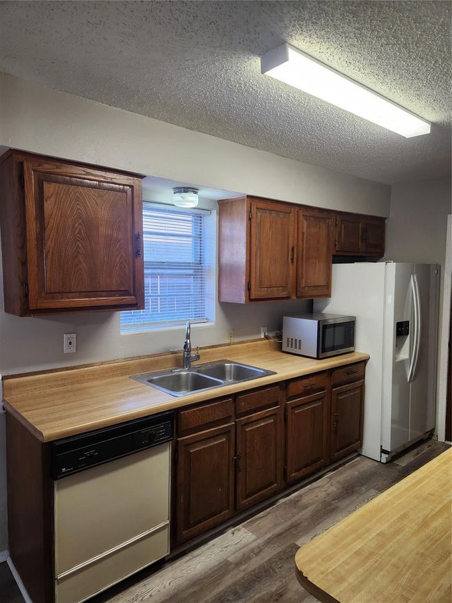 Kitchen featuring dishwasher, stainless steel microwave, a sink, wood finished floors, and a textured ceiling | Image 10