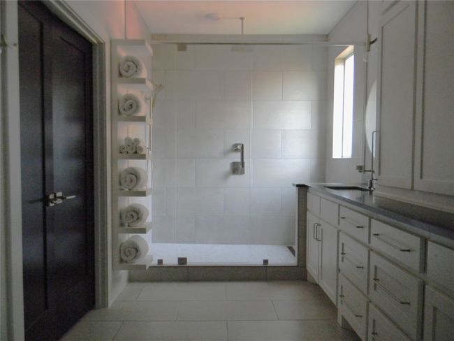 Primary bathroom offers walk-in closet, oversized shower with two shower heads, decorative tile patterned floorin and walls with stone vanity | Image 12