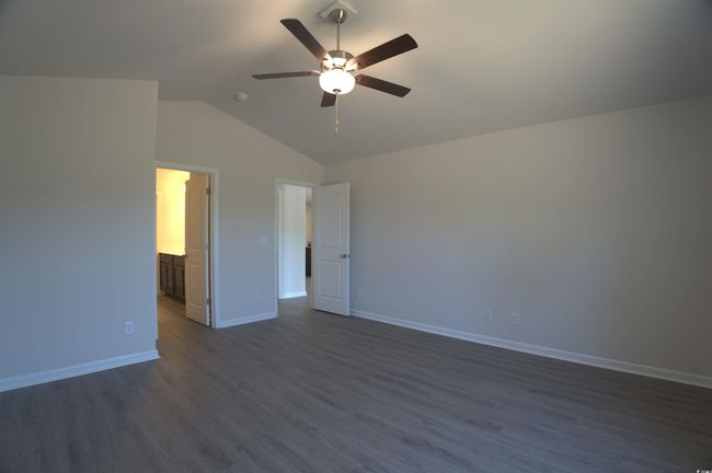Unfurnished bedroom with lofted ceiling, dark wood-style flooring, ceiling fan, and connected bathroom | Image 15