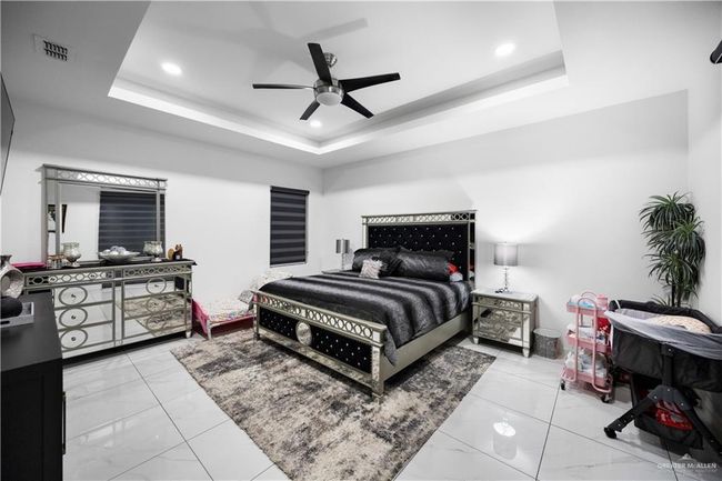 Bedroom with marble look tiles, a tray ceiling, recessed lighting, and ceiling fan | Image 23