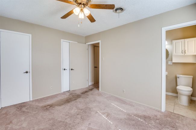 Unfurnished bedroom with ensuite bath, ceiling fan, a textured ceiling, light colored carpet, and multiple closets | Image 22
