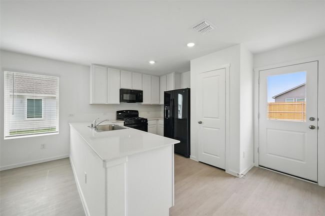 Kitchen with black appliances, light wood finished floors, white cabinetry, light countertops, and healthy amount of natural light | Image 6