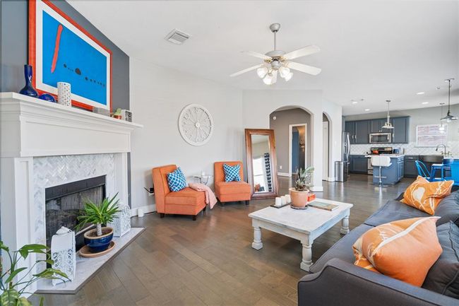 This inviting living room features a cozy fireplace, modern decor, and vibrant pops of color. It opens into a stylish kitchen with gray cabinetry and stainless steel appliances, creating a seamless flow for entertaining. | Image 20