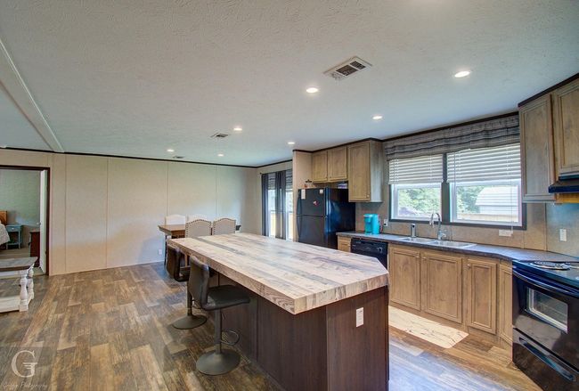 Kitchen with black appliances, wood counters, dark wood-type flooring, a kitchen island, and a breakfast bar | Image 6