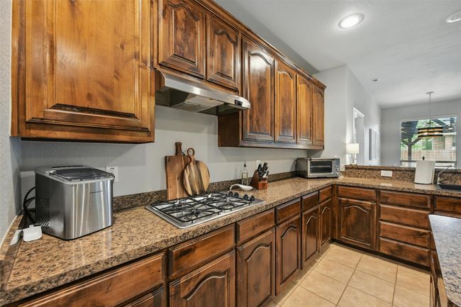 Kitchen with stainless steel gas stovetop, under cabinet range hood, light tile patterned floors, pendant lighting, and stone countertops | Image 21