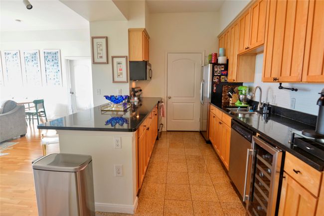 Kitchen featuring a peninsula, beverage cooler, stainless steel appliances, dark stone countertops, and ornamental molding | Image 35