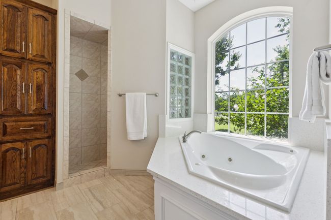 The primary bath offers a large walk in shower, jetted tub and linen cabinet for extra storage. The large window offers natural light and gorgeous views of the lush foliage right outside. | Image 17