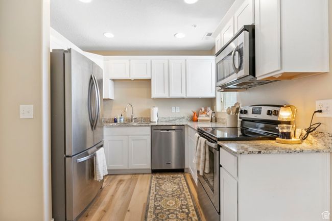 Kitchen featuring light stone counters, white cabinetry, light wood-style floors, appliances with stainless steel finishes, and a sink | Image 12