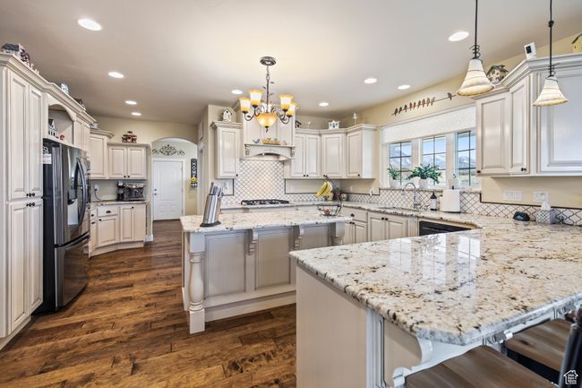 Kitchen featuring dark wood-type flooring, hanging light fixtures, a breakfast bar, a kitchen island, and appliances with stainless steel finishes | Image 26