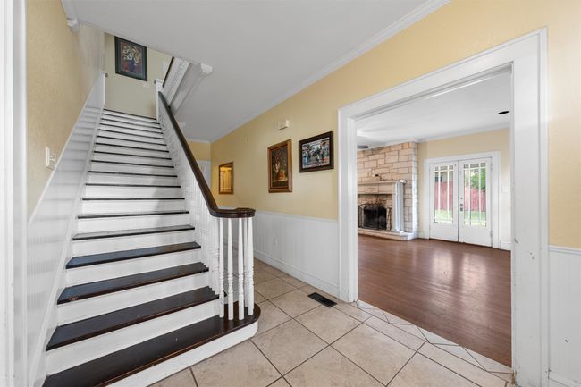Stairs with a wainscoted wall, tile patterned flooring, ornamental molding, a fireplace, and french doors | Image 18