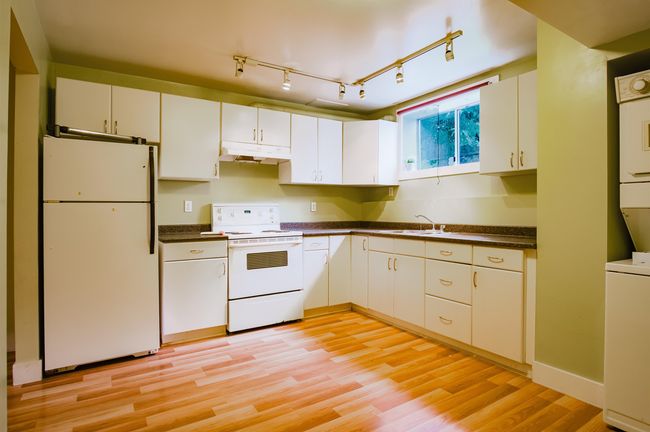 Kitchen with under cabinet range hood, dark countertops, a sink, white appliances, and light wood-style floors | Image 24