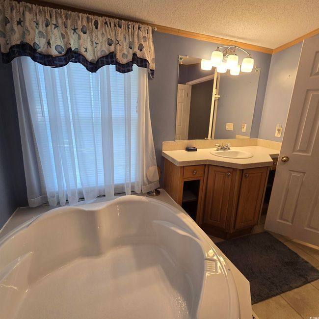 Full bath with vanity, a bathtub, a textured ceiling, ornamental molding, and a chandelier | Image 23