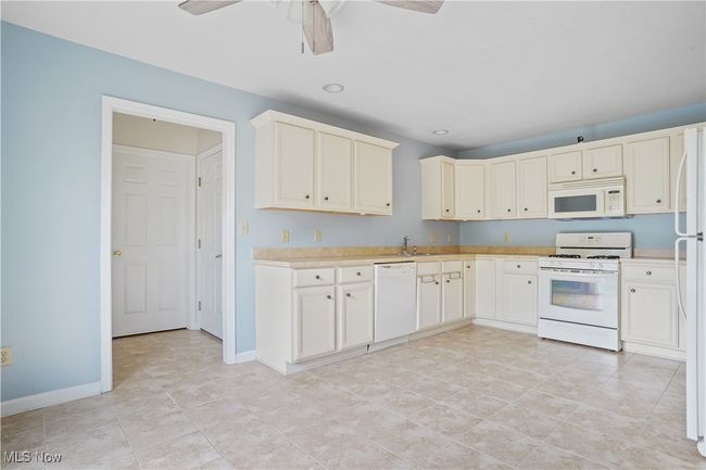 Kitchen with white appliances, light countertops, a ceiling fan, a sink, and baseboards | Image 17