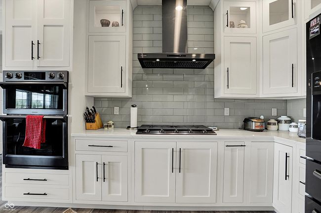 kitchen with black appliances, wall chimney exhaust hood, and white cabinets | Image 16