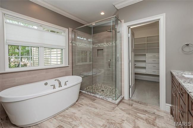 Primary bathroom featuring double vanity, a freestanding tub, a stall shower, ornamental molding, and a spacious walk-in closet | Image 24