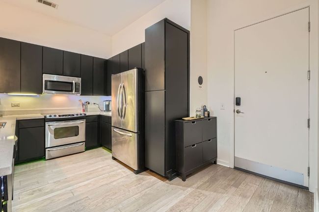 Kitchen featuring light countertops, dark cabinetry, light wood-style flooring, stainless steel appliances, and visible vents | Image 4