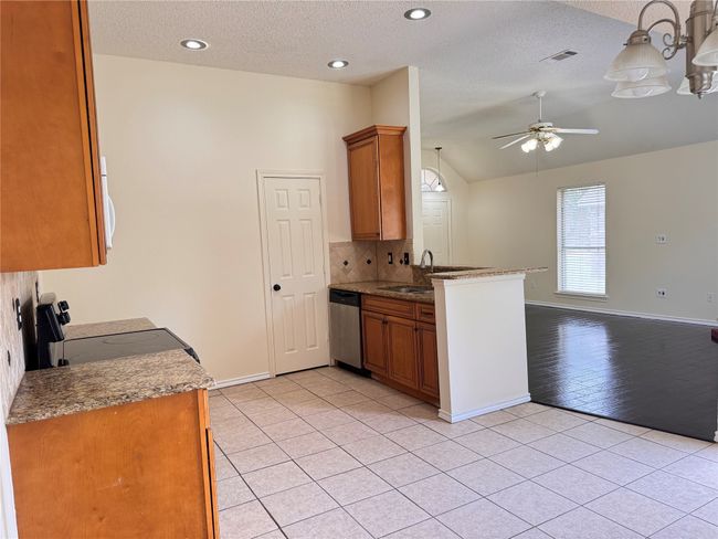 Kitchen with stainless steel dishwasher, a ceiling fan, light tile patterned floors, lofted ceiling, and black / electric stove | Image 15