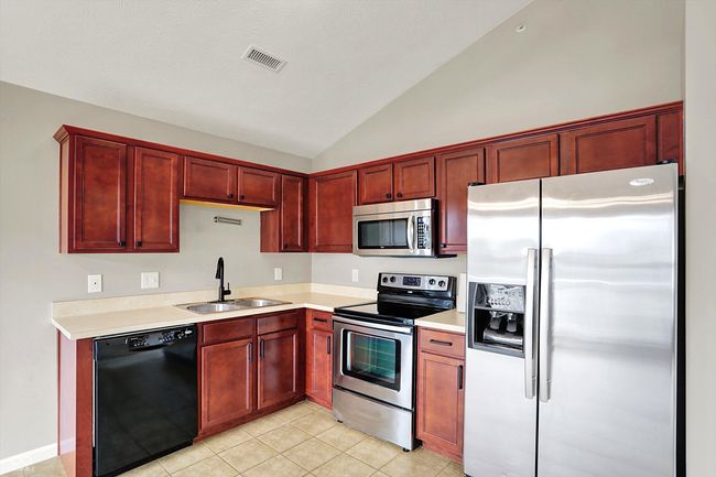 kitchen with appliances, dark reddish brown cabinets, vaulted ceiling, light countertops, and light tile patterned flooring | Image 16