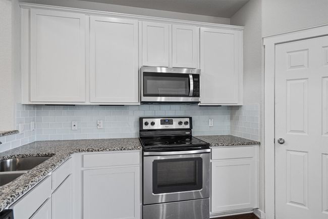Kitchen featuring stainless steel appliances, decorative backsplash, white cabinets, and stone counters | Image 18