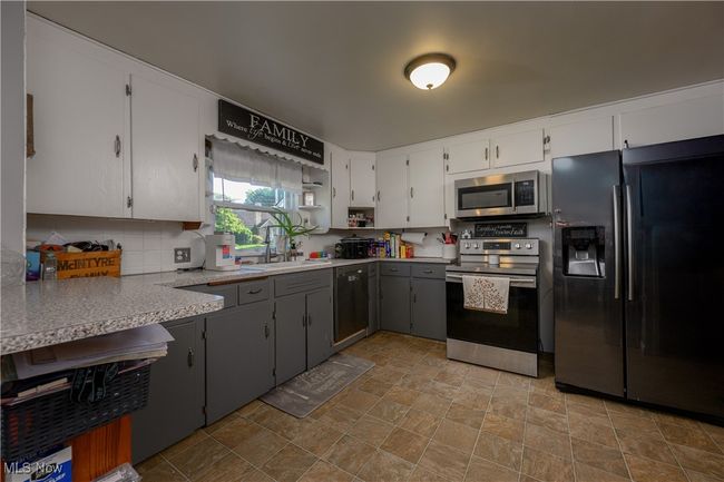 Kitchen featuring stainless steel appliances, stone finish floors, backsplash, light countertops, and white cabinets | Image 11